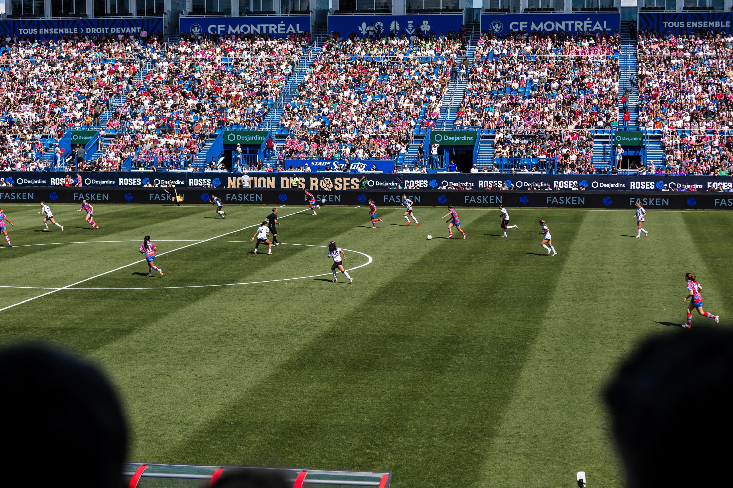 A packed Stade Saputo watches a Montréal Roses match from the stands, Nation des Roses hoardings ringing the pitch.